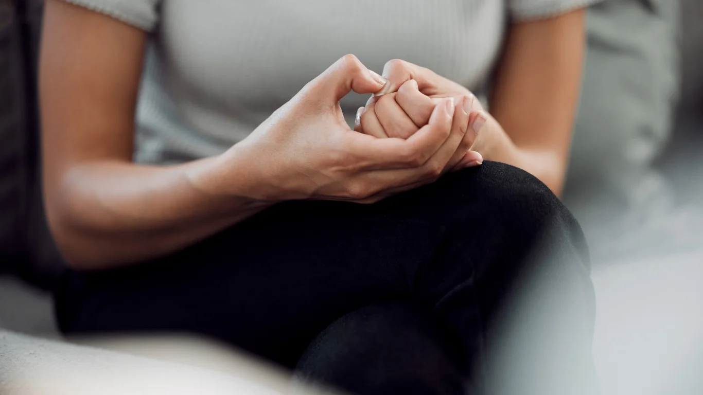 a woman sits on a couch holding her hands together