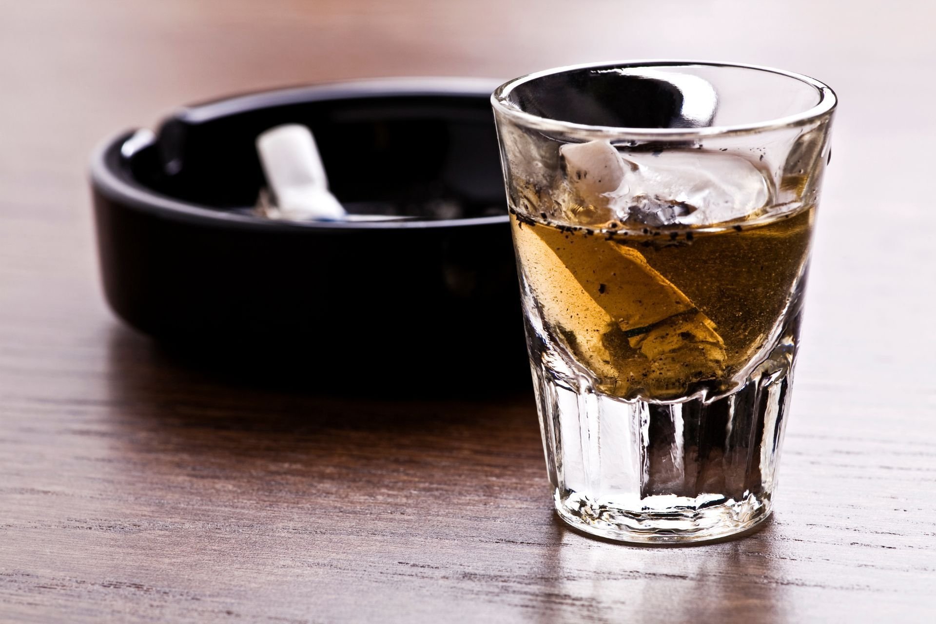 an ashtray with a cigarette butt and a shot glass with liqour on a table
